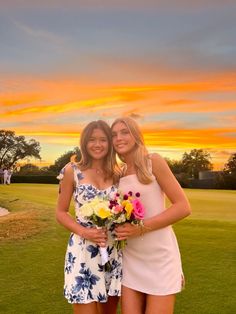 two beautiful young women standing next to each other on top of a grass covered field