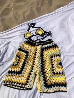 a crocheted yellow and black shorts laying on top of a white bed sheet