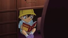 an anime character sitting on the floor reading a book in front of a wooden cabinet