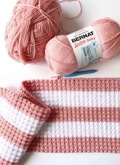 two balls of yarn next to each other on top of a white and pink blanket