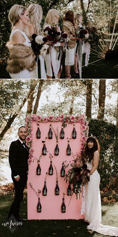 a couple standing next to each other in front of a pink wall with wine bottles on it