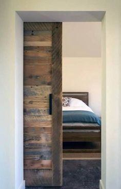 an open door leading to a bedroom with a bed in the background and wood planks on the wall