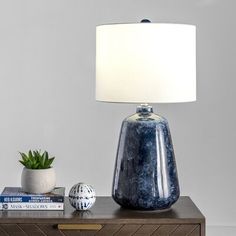 a blue vase sitting on top of a wooden table next to a lamp and books