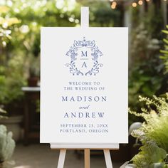 an easel with a wedding welcome card on it sitting in front of some plants