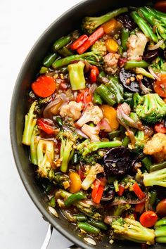 a skillet filled with vegetables and meat on top of a white countertop next to utensils