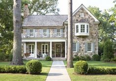 a large stone house with white trim and shutters in the front yard, surrounded by trees