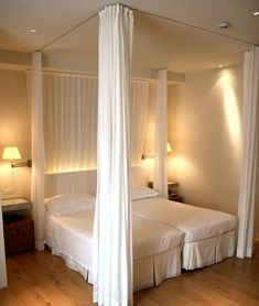 two beds with white drapes on them in a bedroom next to lamps and wood flooring