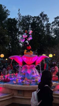 people are standing around in front of a fountain with lights and characters on it at night