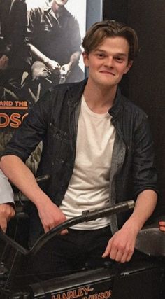 a young man sitting on top of a black motorcycle in front of a movie poster