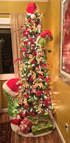 a decorated christmas tree in the corner of a room with santa hats on top and presents under it