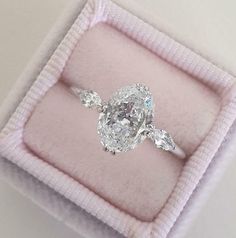 an oval diamond ring with three pear shaped diamonds on it in a pink velvet box