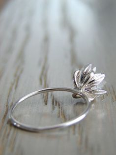 a silver ring with a flower on it sitting on top of a wooden table next to a piece of wood