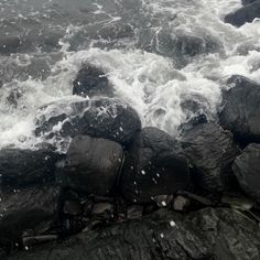 the water is rushing over some rocks in the ocean with white foam on it's surface