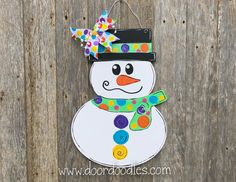 a snowman door hanger hanging on a wooden fence with polka dots and a bow