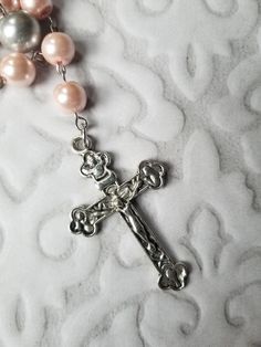 This Lutheran rosary has silver-toned findings and glass pearl beads in pink and gray. I used larger beads than I normally do on this one. It's really pretty. This rosary is hand-wired using silver-tone eye pins and my trusty little looper tool. The beads are connected by these loops. In the rosary itself, the small beads are 10mm pink glass pearls. The large beads are 12mm silver gray glass pearls. At the end of the stem is a silver-toned, budded metal crucifix. It measures 57mm x 35mm. 25.4 mm Silver Beaded Rosary For First Communion, Adjustable Silver Crucifix Rosary, Silver Pearl Rosary With 8mm Beads, Handmade Silver Rosary Bracelet For First Communion, Silver Pearl Rosary For First Communion, Silver Beaded Rosary With Spiritual Style, Silver Beaded Spiritual Rosary, Adjustable Silver Pearl Rosary, Spiritual Silver Beaded Rosary