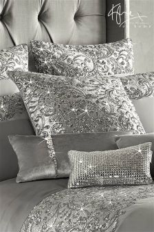 black and white photograph of a bed with silver comforter, pillows and headboard