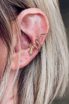 A woman wearing a gold snake ear cuff earring. Trendy Adjustable Wrap Earrings Gift, Adjustable Metal Trendy Ear Cuff, Trendy Adjustable Pierced Ear Climbers, Adjustable Trendy Ear Climbers, Trendy Adjustable Wrap Earrings, Trendy Internally Threaded Ear Cuff As Gift, Edgy Adjustable Cartilage Earrings For Gift, Adjustable Edgy Cartilage Earrings For Gift, Adjustable Trendy Snake Jewelry