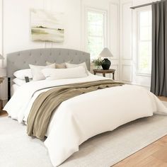 a bedroom with white walls and wood flooring has a gray headboard on the bed