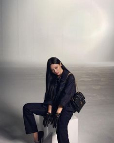 a woman sitting on top of a white block wearing black gloves and holding a handbag