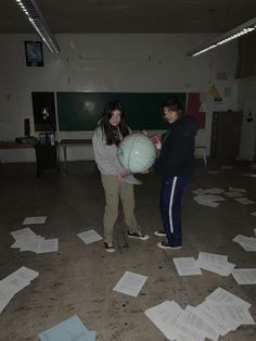 two people standing in an empty room with papers all over the floor and one person holding a globe