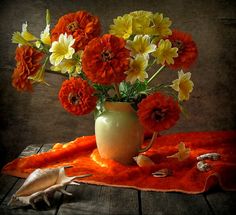 a white vase filled with orange and yellow flowers on top of a wooden table next to shells