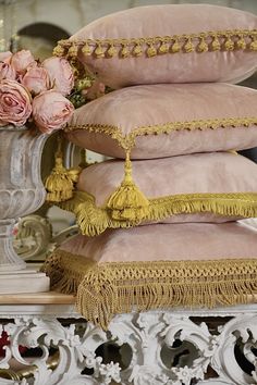 four pillows stacked on top of each other with tassels and flowers in the background