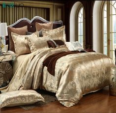 a large bed covered in gold and brown comforter sets on a wooden floor next to a window