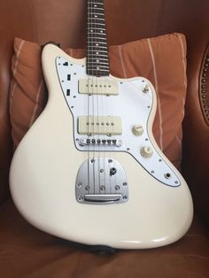 a white electric guitar sitting on top of a brown leather couch next to a pillow