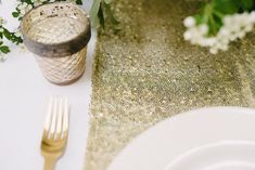 the table is set with white and gold plates, silverware, and greenery