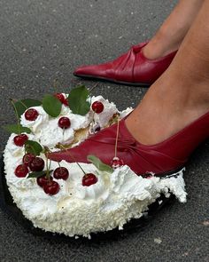 a woman wearing red shoes standing on top of a cake with cherries and whipped cream