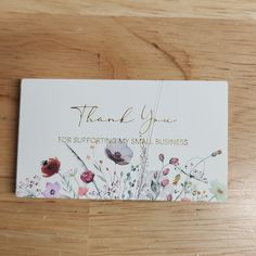 a thank card with flowers on it sitting on top of a wooden table next to a pen