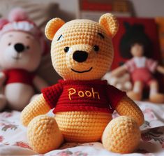 two crocheted teddy bears sitting on a bed next to each other and one is wearing a shirt that says pooh