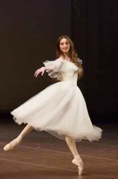 a woman in a white dress is dancing on a stage with her arms outstretched and legs spread out