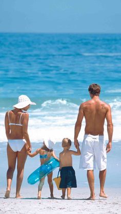 a man, woman and two children are walking on the beach with their surfboards