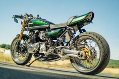 a green and black motorcycle parked on the side of the road with grass in the background