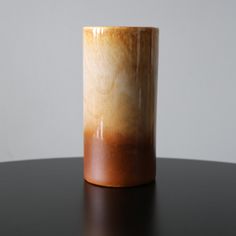 a brown and white vase sitting on top of a black table next to a gray wall