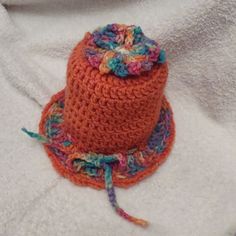 an orange crocheted hat with a colorful flower on top sits on a white blanket