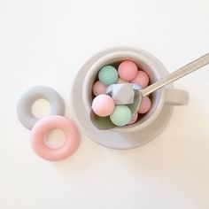 a cup filled with donuts and candy on top of a white table next to a spoon