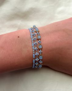 a woman's arm is covered in blue beaded bracelets with gold beads