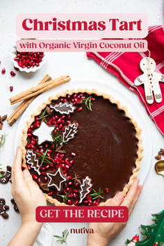 a person holding a chocolate tart on top of a white plate with christmas decorations