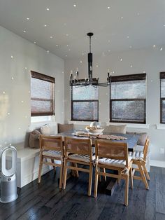 a dining room table and chairs in front of two windows with lights on the ceiling