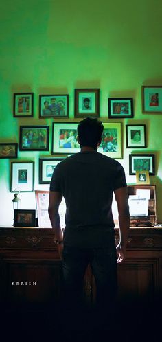 a man standing in front of a green wall with many pictures on the wall behind him