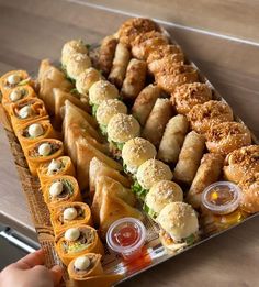 a tray filled with lots of food on top of a wooden table next to a person's hand