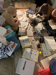 several people sitting at a table with books and notebooks on it, all covered in paper