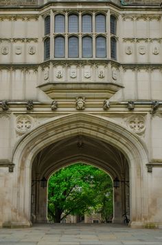 an archway leading into a building with trees in the foreground and stone walkway on either side