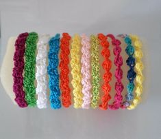 several crocheted bracelets are lined up on a white surface, one is multicolored