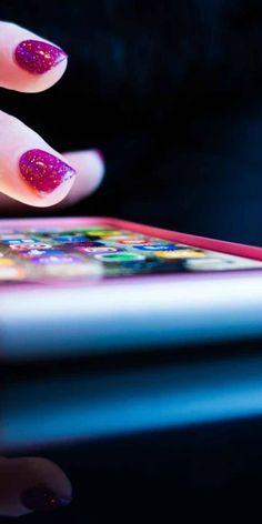 a woman's hand with pink and purple glitter on her nails touching an ipad