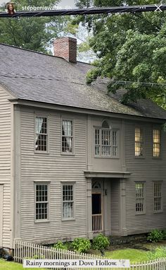 an old gray house with a white picket fence around it and trees in the background