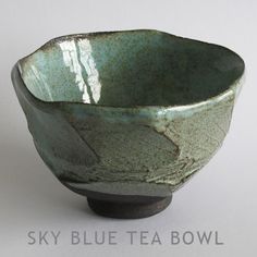 a green bowl sitting on top of a white table next to a black cup with the word sky blue tea bowl written below it