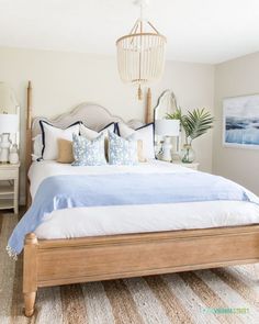 a bed with blue and white pillows on top of it next to a lamp hanging from the ceiling